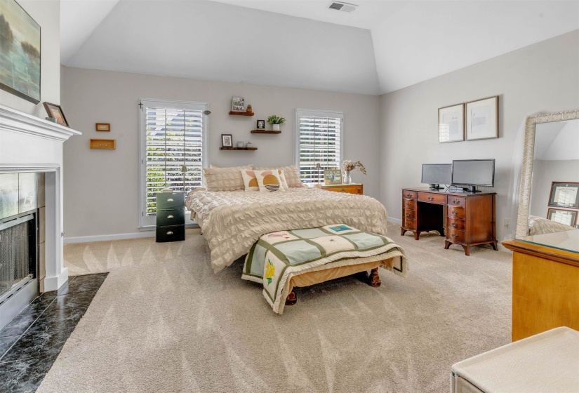 Bedroom featuring vaulted ceiling, carpeted flooring, and a white mantel fireplace with a dark stone hearth