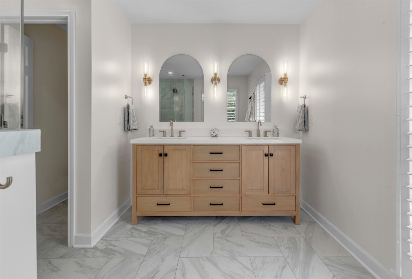 Dual vanity featuring a wood-finish cabinet with black hardware, white countertop, and two arched mirrors