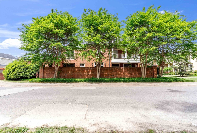Brick exterior residence featuring a second-story balcony with white railing, a low brick privacy wall, and mature deciduous trees