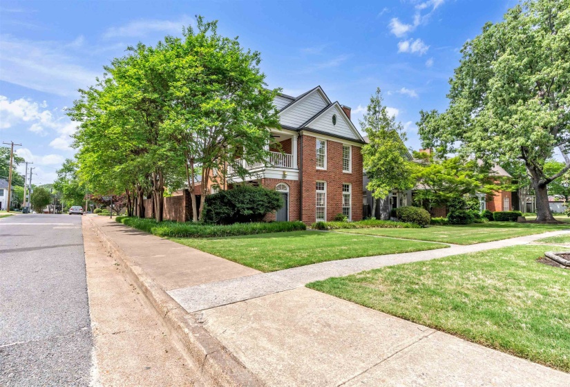 Brick facade home featuring a white-trimmed gable, second-story balcony, and mature trees