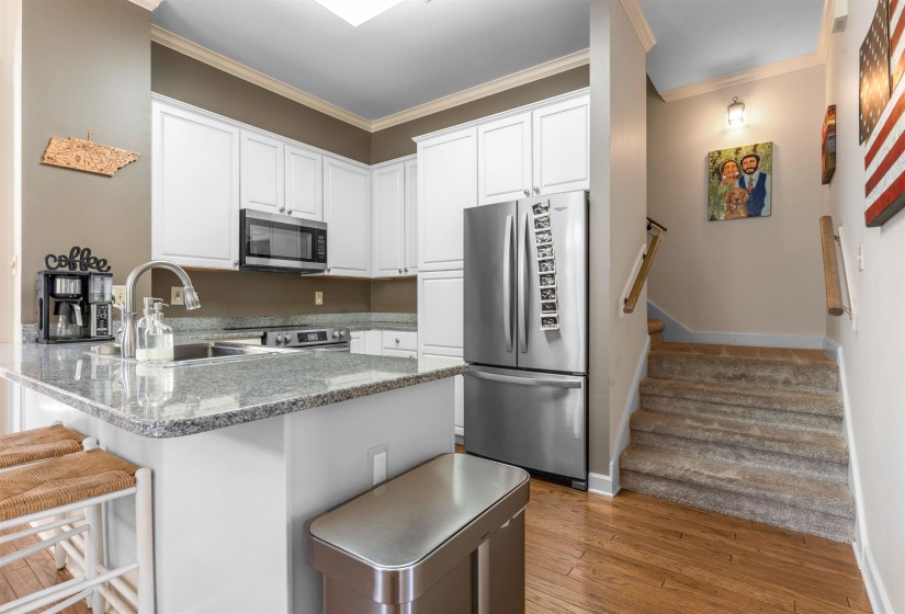Kitchen featuring white shaker cabinetry, stainless steel appliances, granite countertops, and wood-finish flooring
