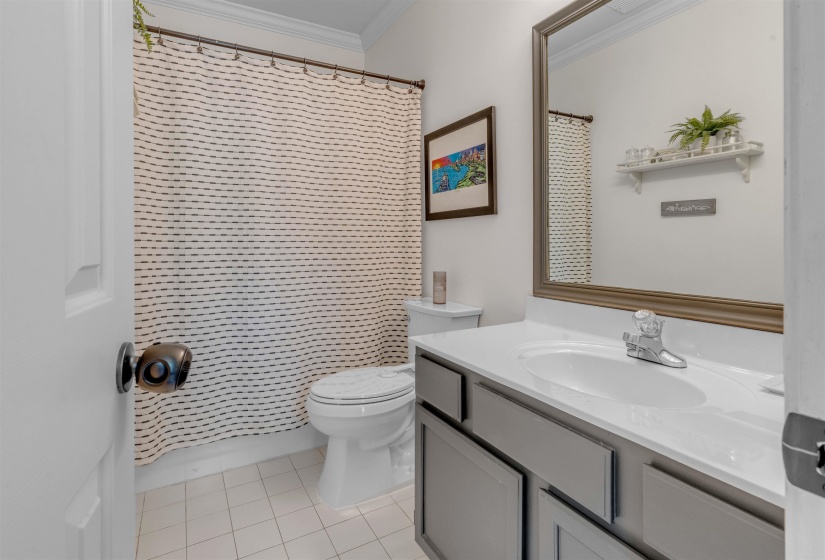 Bathroom featuring a single vanity with a white countertop and integrated sink, a large framed mirror, a toilet, and white square tile flooring
