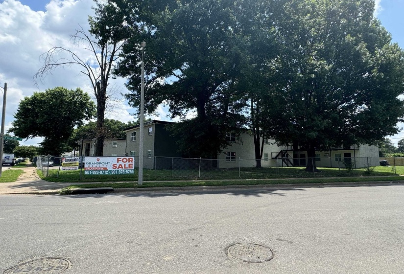 Multi-unit residential structure featuring a neutral-toned exterior, multiple windows, and a surrounding chain-link fence