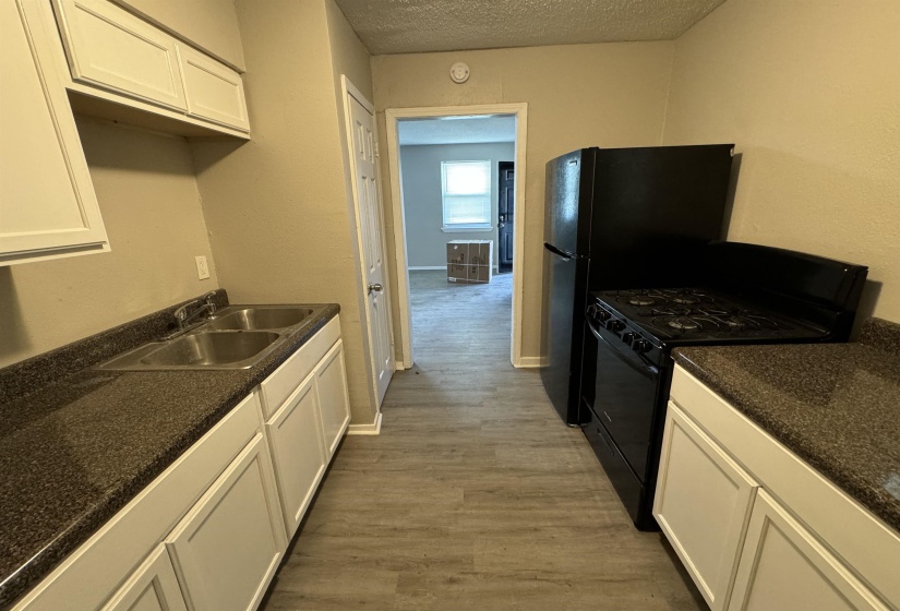 Kitchen featuring white cabinetry, dark speckled countertops, a double basin stainless steel sink, black refrigerator, and a black range