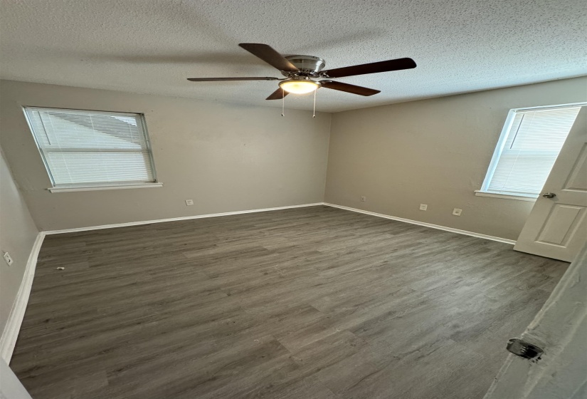 Room featuring wood-finish flooring, two windows with blinds, a ceiling fan with integrated lighting, and neutral wall paint