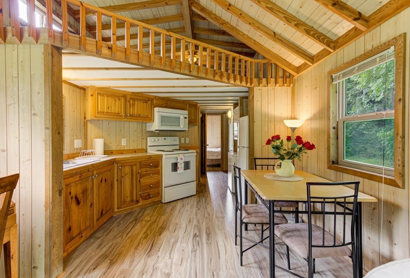 Open-concept kitchen and dining area featuring wood-finish flooring, natural wood cabinetry, a white appliance suite, and exposed wood beam vaulted ceilings