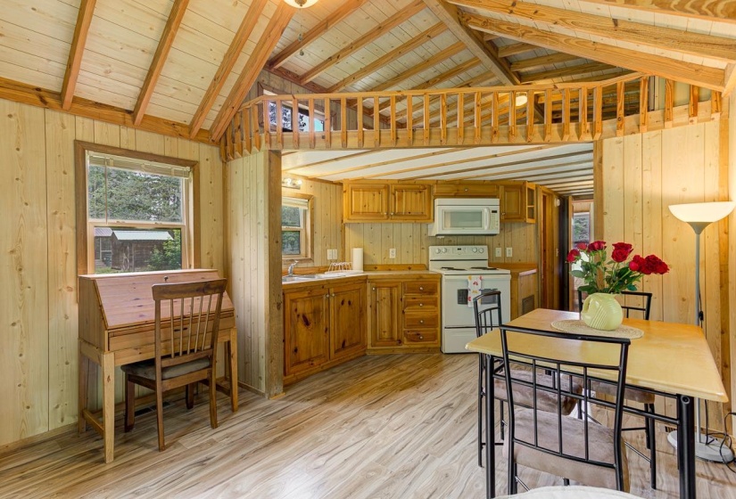 Open-concept living space featuring wood-finish flooring, natural wood paneled walls, and a vaulted ceiling with exposed beams
