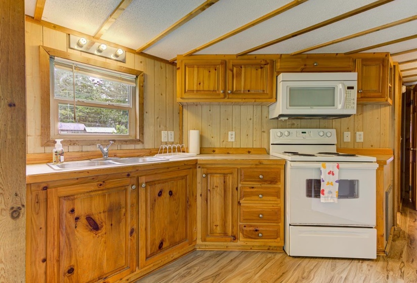 Kitchen featuring natural wood cabinetry, light countertops, wood-finish flooring, a white electric range, and an over-the-range microwave