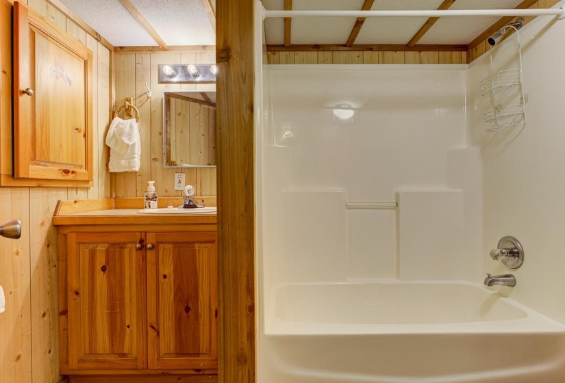 Bathroom featuring wood-paneled walls and ceiling, a wood-finish vanity with an integrated sink, a mirrored wall cabinet, and a white fiberglass tub/shower combination