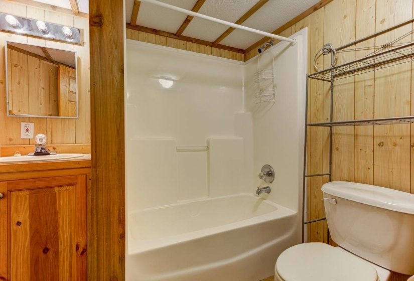 Bathroom featuring a white tub and shower combination, wood-paneled walls, a single vanity with a white sink, and a mirrored medicine cabinet