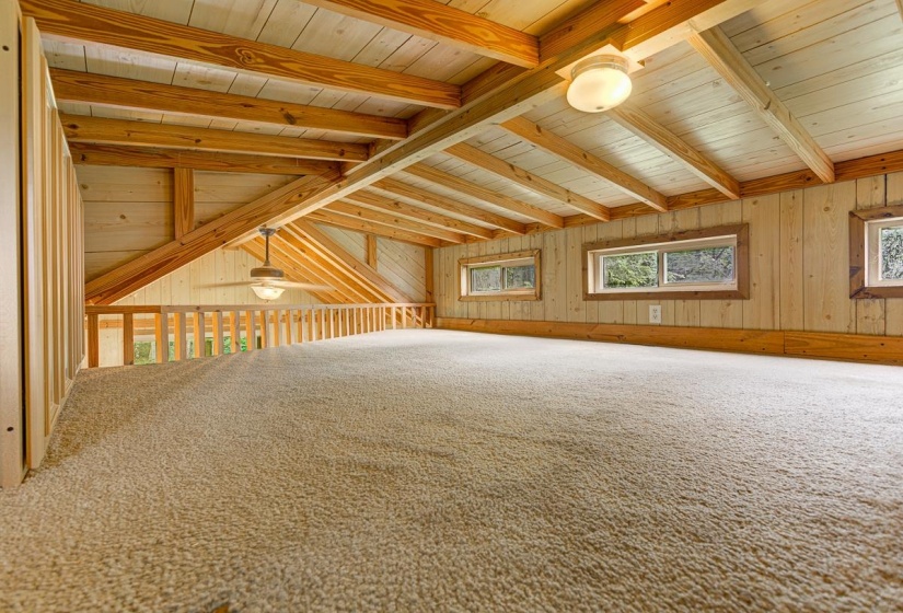 Carpeted loft area featuring exposed wood beams and paneling
