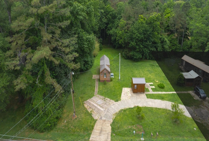 Expansive green space featuring a compact cabin, a separate utility building, concrete pathways, and mature trees surrounding the property