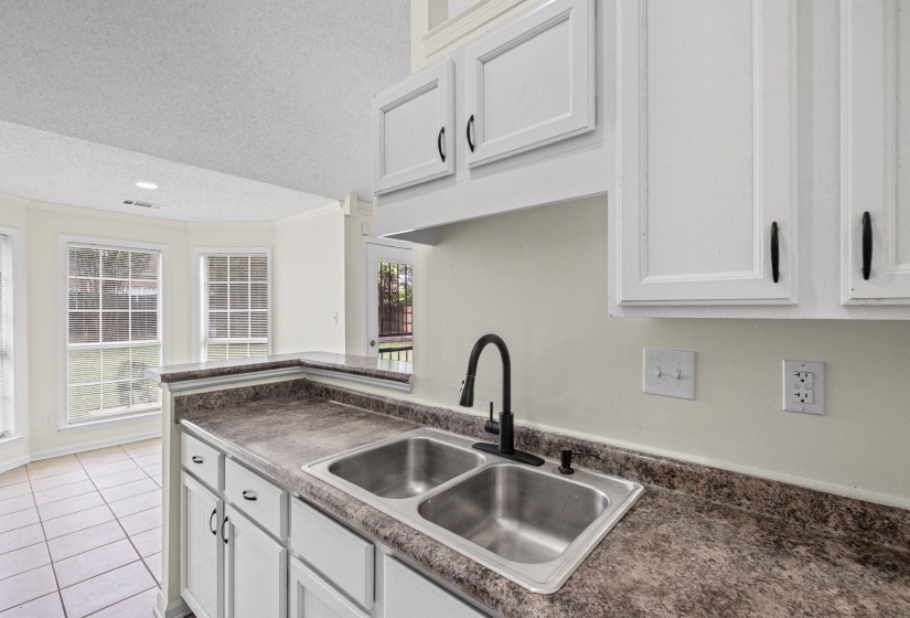 Kitchen featuring white cabinetry, a dual basin stainless steel sink with a matte black faucet, and patterned laminate countertops