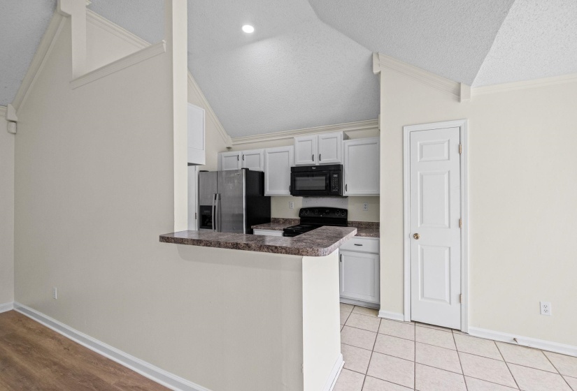 Kitchen area featuring white cabinetry, black appliances, a breakfast bar with a stone-finish countertop, and tiled flooring