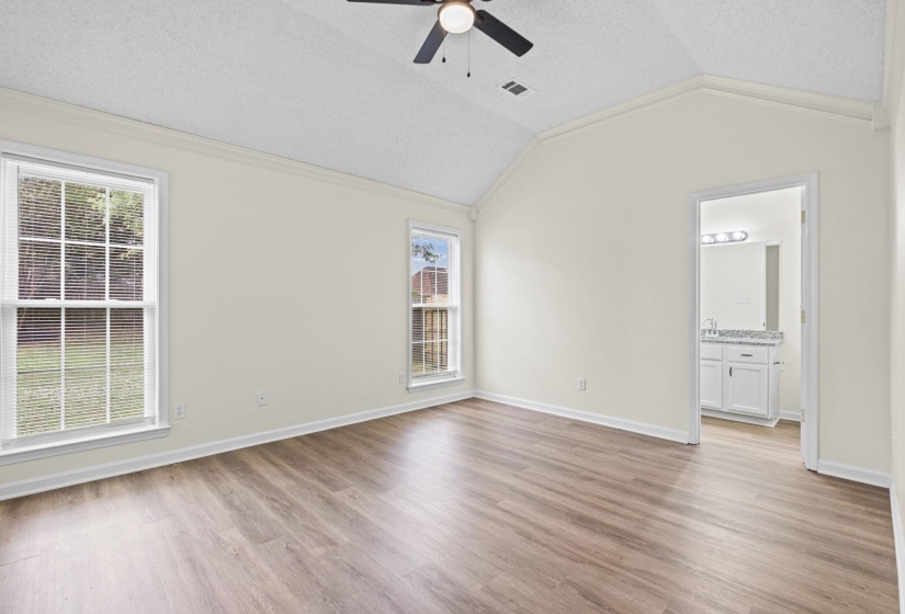 Vaulted ceiling room featuring wood-finish flooring, two windows with blinds, and a ceiling fan