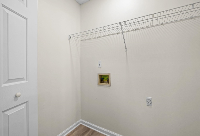 Dedicated utility space featuring a wire shelving unit, electrical outlets, and wood-finish flooring with baseboards