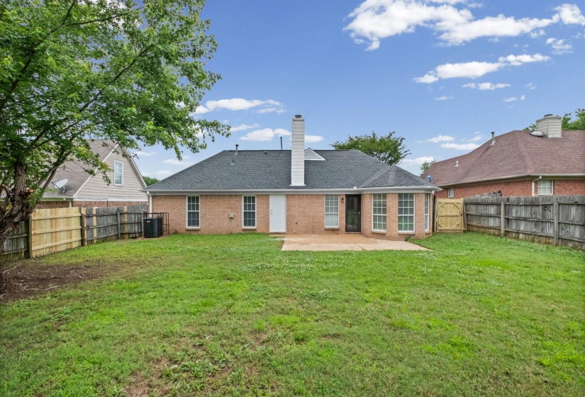 Expansive backyard with a manicured lawn, perimeter fencing, mature trees, and a concrete patio