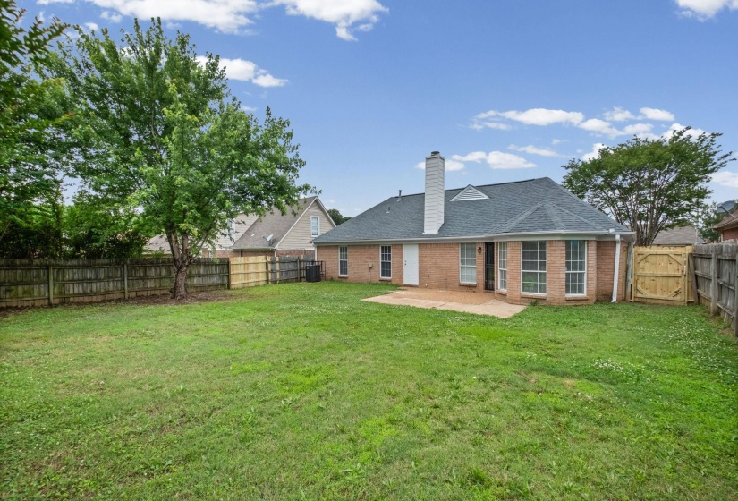 Spacious rear yard with a mature tree, privacy fencing, and a brick patio