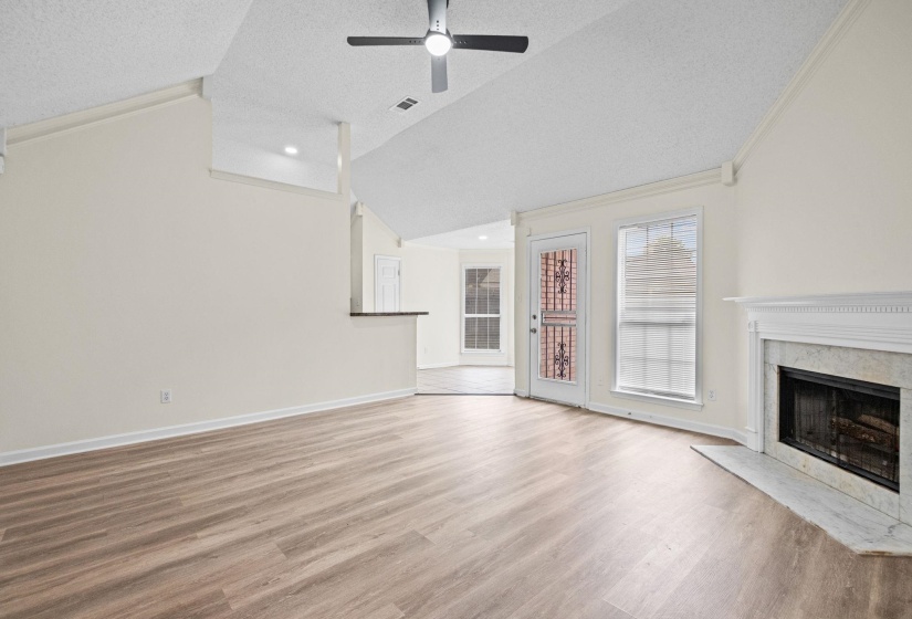 Spacious living area featuring wood-finish flooring, a vaulted ceiling, and a ceiling fan