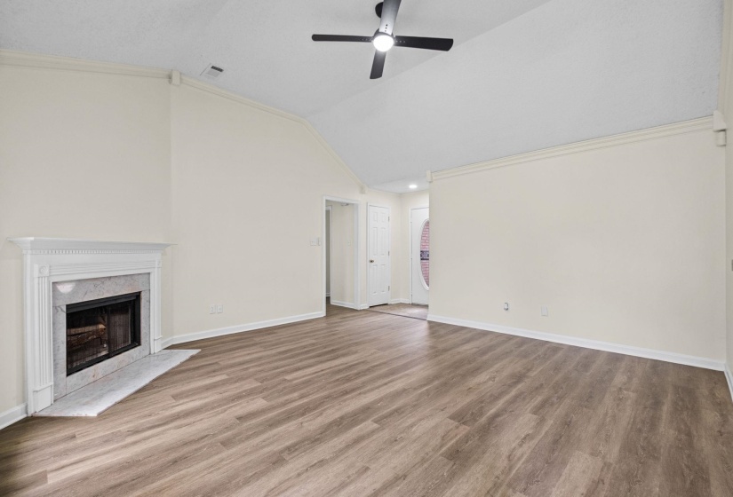 Living area featuring wood-finish flooring, a white mantel fireplace with a stone surround, vaulted ceilings, and a ceiling fan