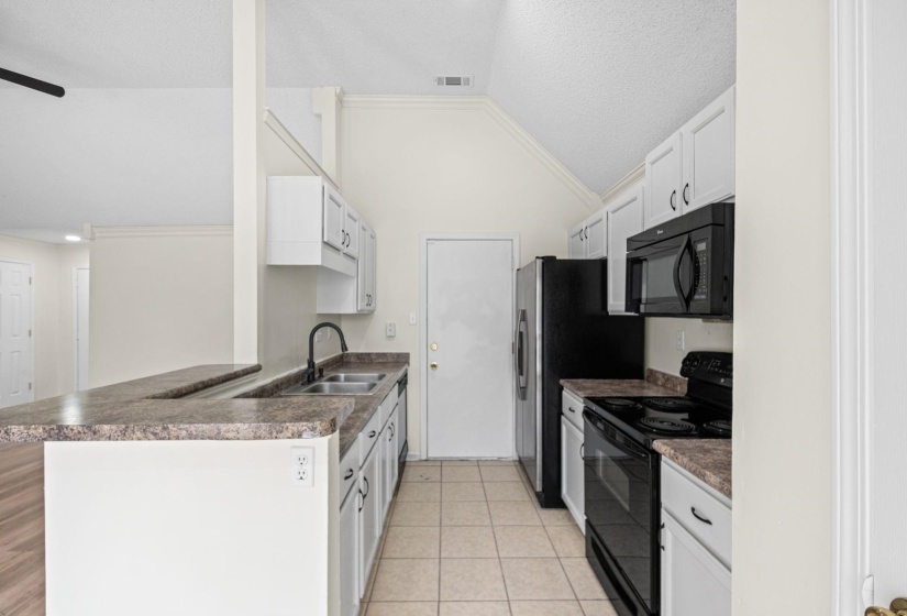 Kitchen featuring white cabinetry, dark countertop surfaces, black appliances, a double basin sink with a matte black faucet, and tile flooring