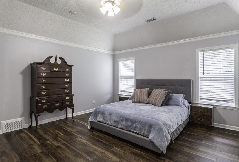 Spacious room featuring wood-finish flooring, vaulted ceiling, and crown molding