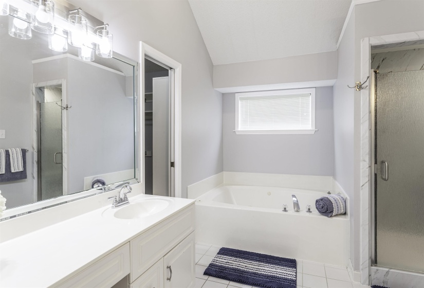 Dual vanity with an integrated sink and chrome faucet, a large soaking tub with chrome fixtures, and a glass-enclosed shower featuring tile surround