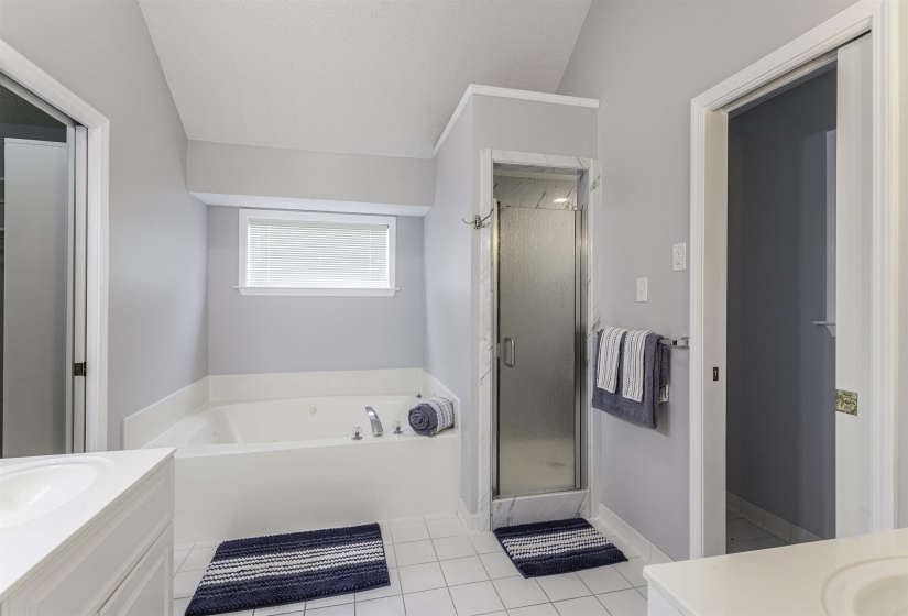 Contemporary bathroom featuring a jetted tub, a separate glass-enclosed shower, dual vanity sinks, white tile flooring, and a window with horizontal blinds