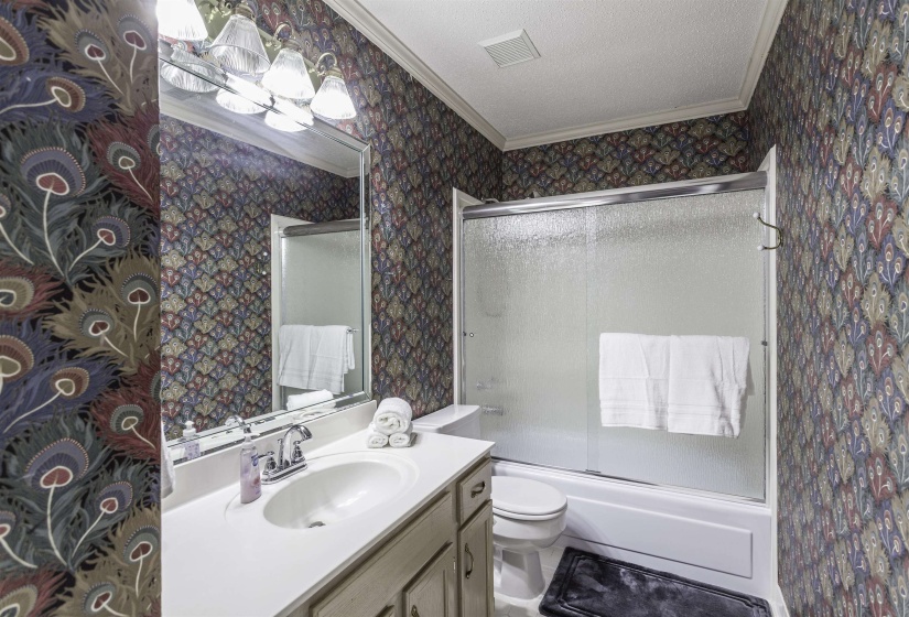 Full bathroom featuring a single vanity with an integrated sink, a large wall-mounted mirror, and a shower-tub combination with sliding frosted glass doors