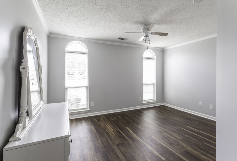 Room featuring two arched windows with blinds, wood-finish flooring, and a ceiling fan with integrated lighting