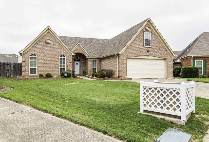 Brick facade residence featuring a front-facing garage with a white door, arched and rectangular windows, a covered front entry, and a green lawn