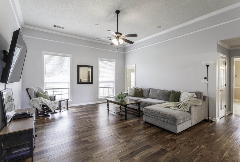 Spacious living area featuring rich wood-finish flooring, a vaulted ceiling with crown molding, and a ceiling fan