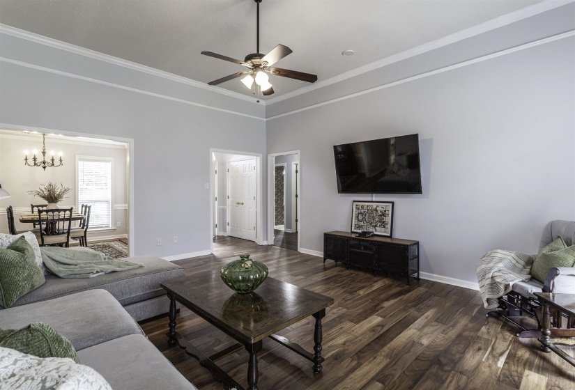 Spacious living area featuring wood-finish flooring, vaulted ceilings with crown molding, and a ceiling fan with integrated lighting