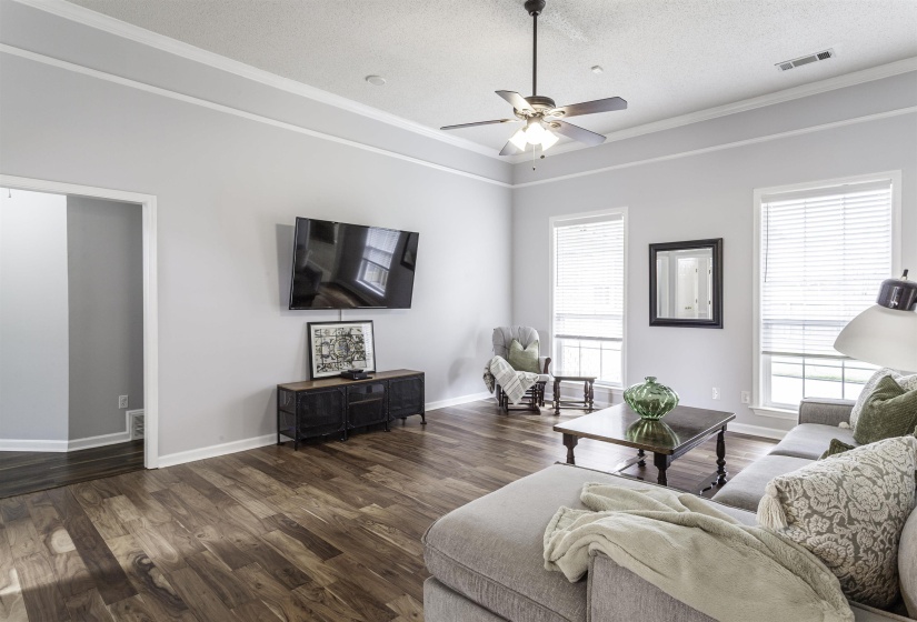 Spacious living area featuring wood-finish flooring, a tray ceiling, and white crown molding