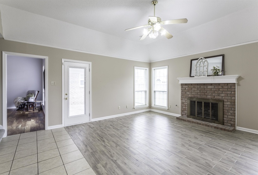 Spacious living area featuring a brick fireplace with a white mantel, high vaulted ceilings, and wood-finish flooring