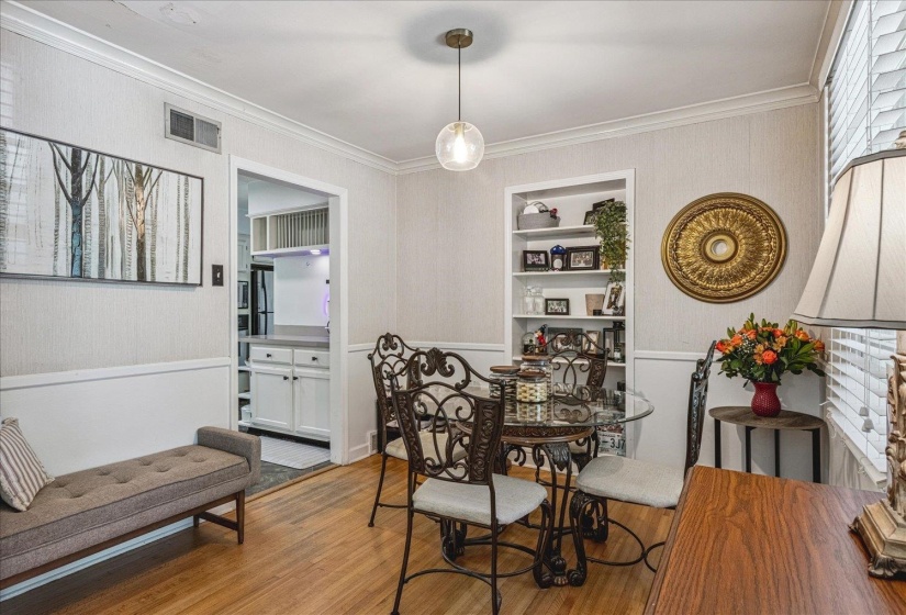 Dining area with wood-finish flooring, built-in shelving, crown molding, and wainscoting