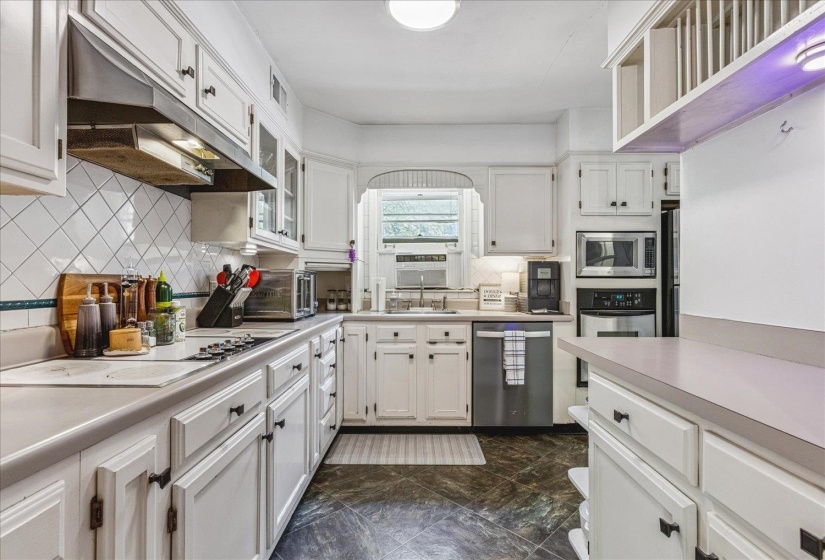 White cabinetry with dark hardware, a tile backsplash, and dark-finish flooring define this kitchen