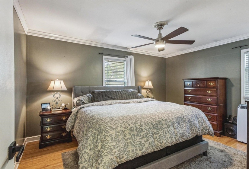 Bedroom featuring wood-finish flooring, a ceiling fan with integrated lighting, crown molding, and a window with blinds