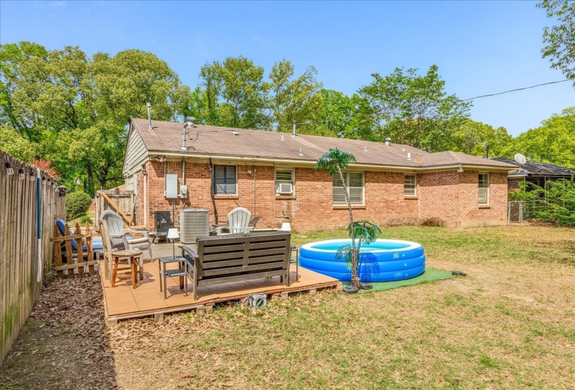 Expansive backyard featuring a brick exterior, a wood deck, a partial wood fence, and mature trees surrounding the property