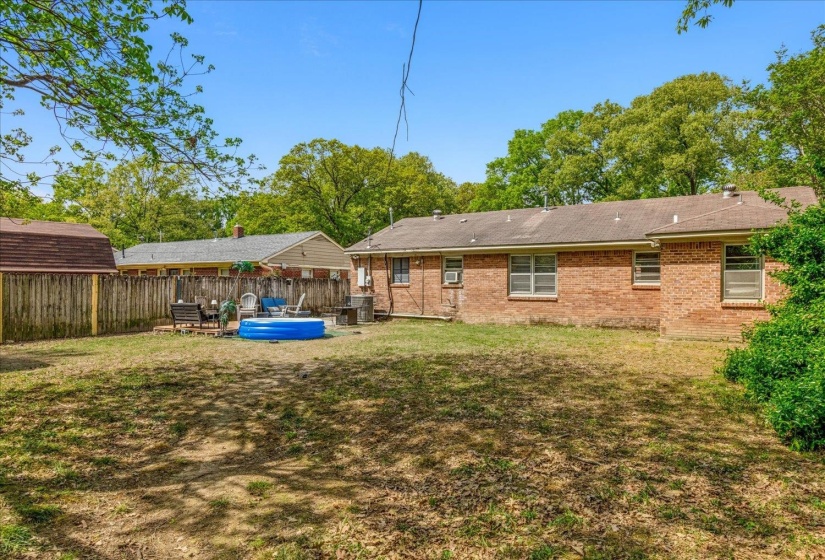 Expansive backyard featuring a brick exterior, a wooden privacy fence, mature trees, and a storage shed