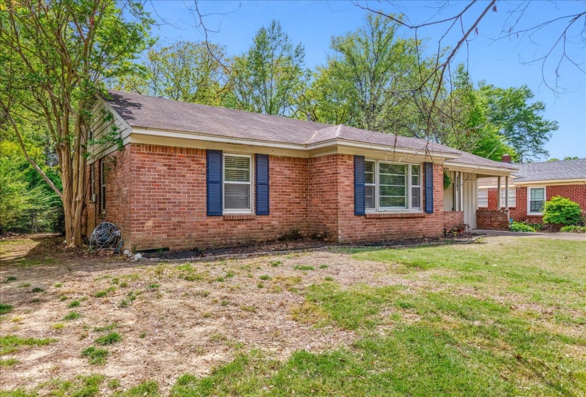 Traditional brick exterior featuring blue window shutters, a covered porch entrance, and mature landscaping