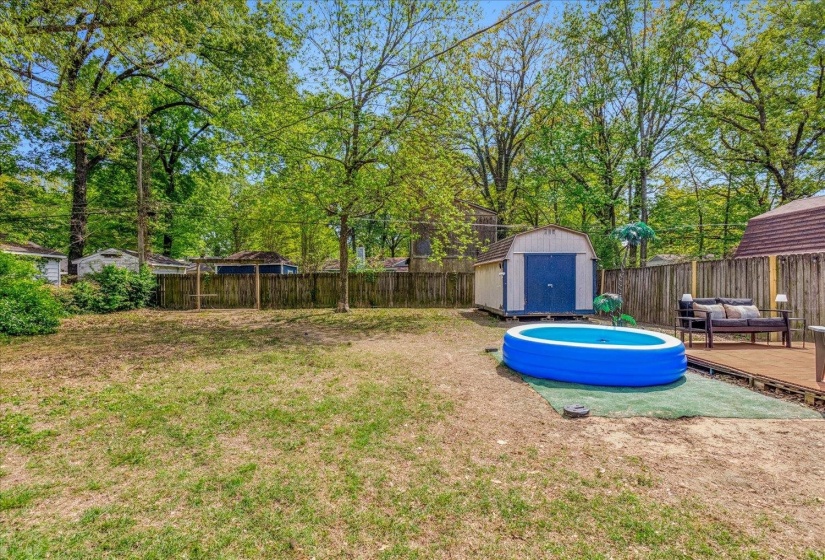 Spacious backyard featuring a wooden privacy fence, a detached storage shed, and a wooden deck