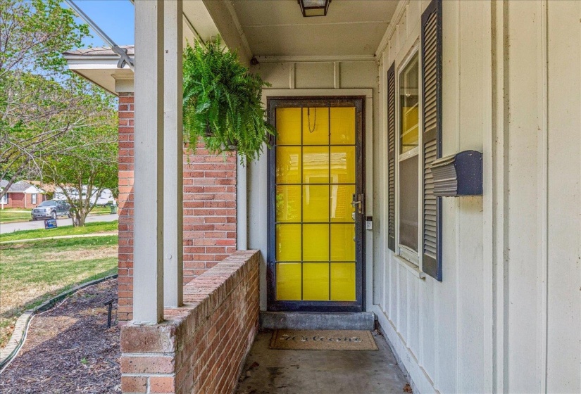 Front porch entry with a yellow grid-pattern storm door, white vertical siding, and brick accents