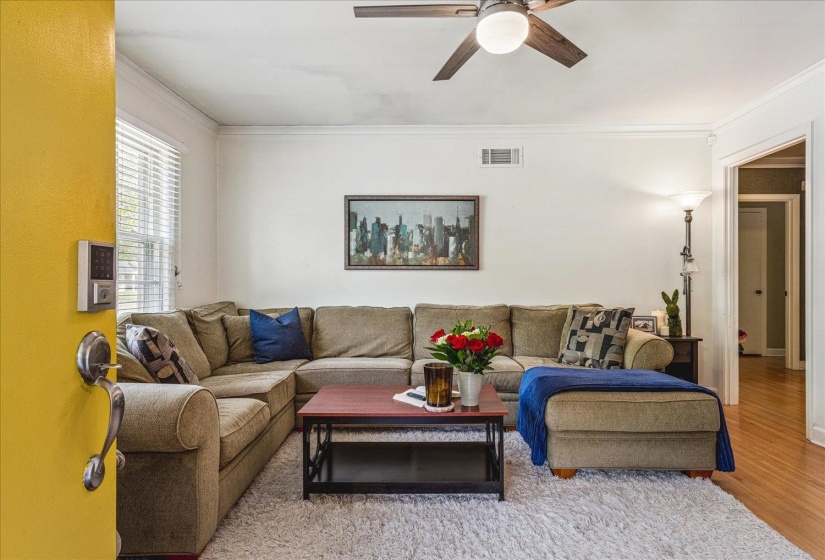 Bright living space featuring a ceiling fan, crown molding, and wood-finish flooring