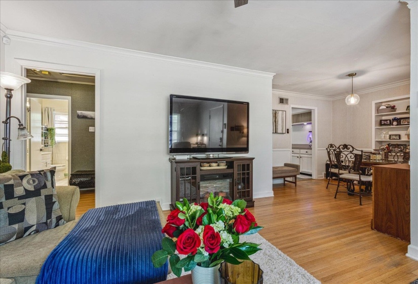 Hardwood flooring extends throughout this expansive living area, featuring crown molding and a built-in media console