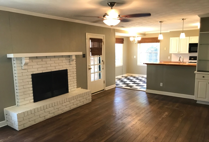 Living area featuring wood-finish flooring, a painted brick fireplace with a mantel, and a ceiling fan