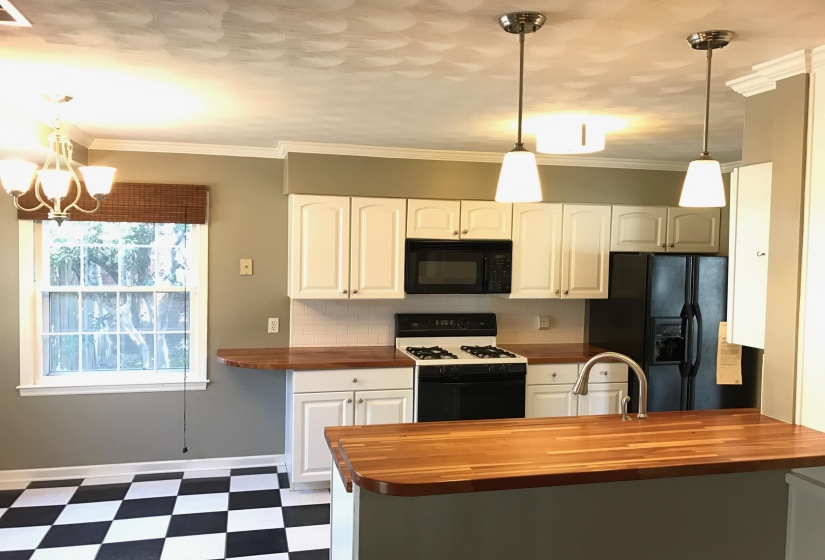Kitchen featuring white cabinetry, butcher block countertops, stainless steel sink with gooseneck faucet, black and white checkered flooring, and pendant lighting
