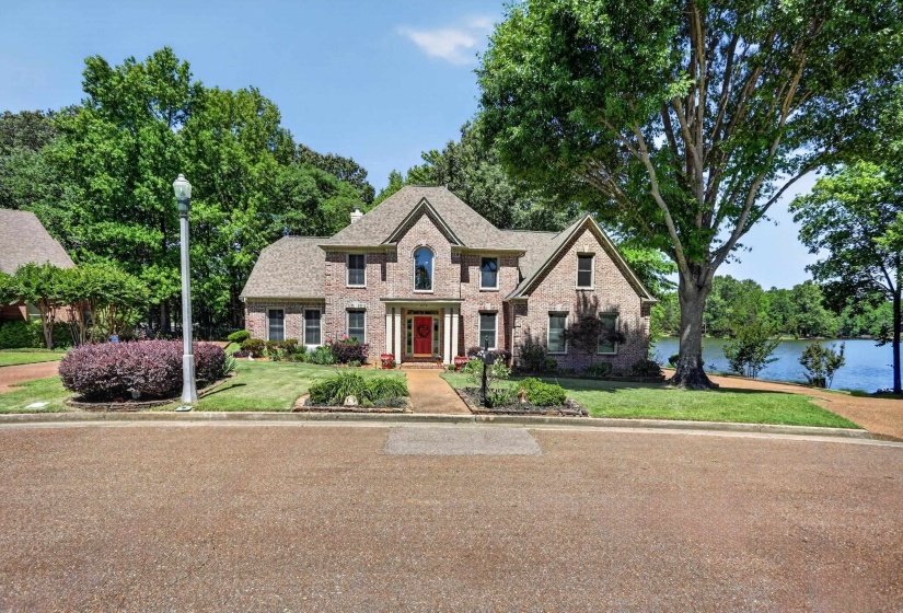 Brick facade residence featuring a prominent red entry door, a multi-gabled roofline, and beautiful established landscaping