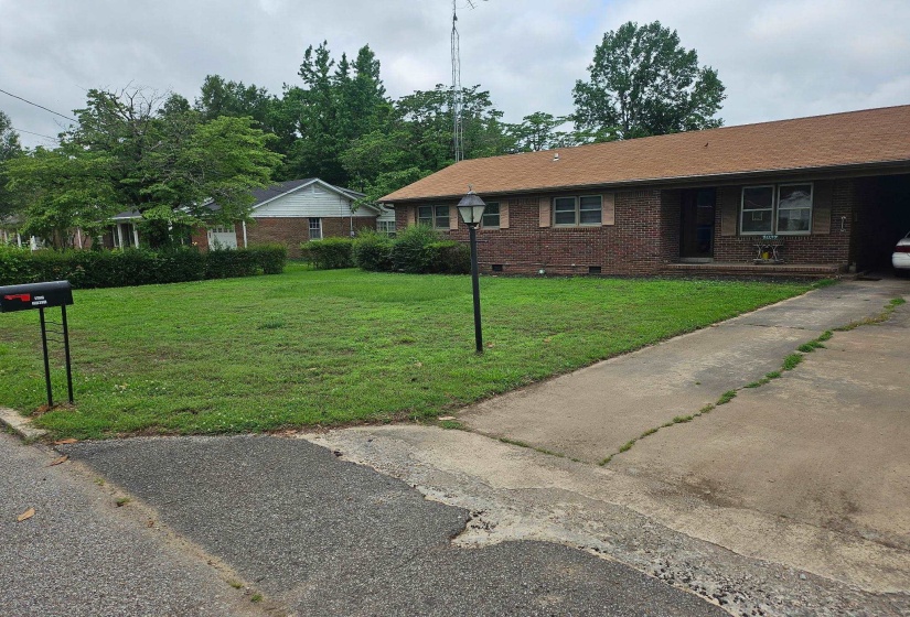 Brick ranch-style residence featuring a brown shingle roof, a concrete driveway, and a front lawn with mature landscaping