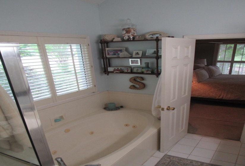 Jetted soaking tub with a window featuring white plantation shutters